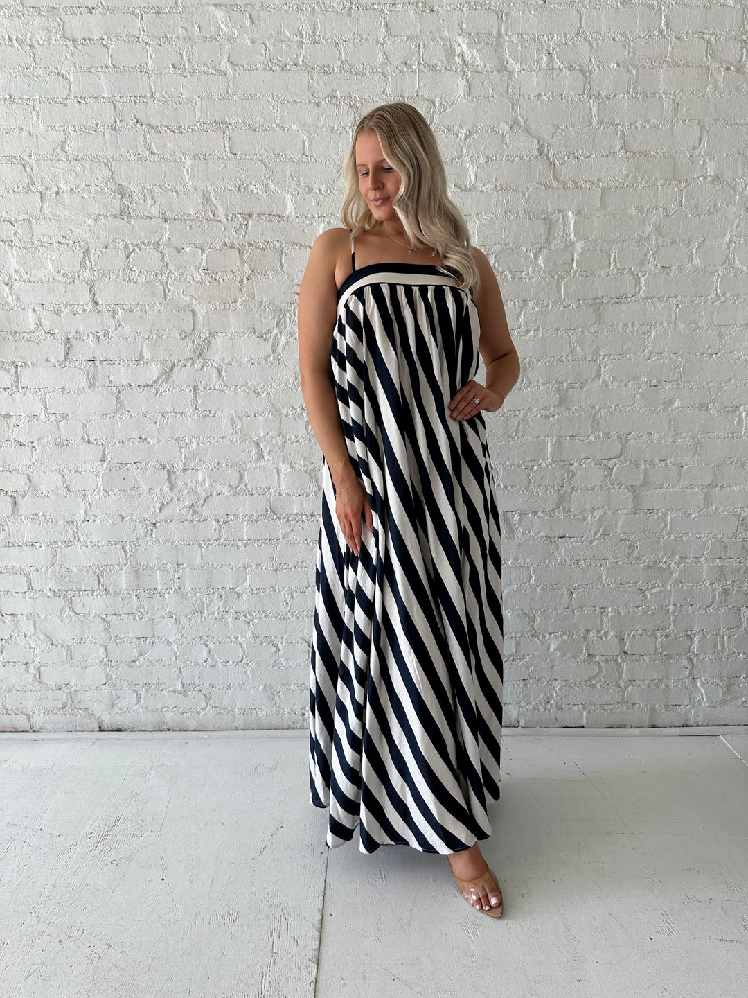 Woman wearing navy and white striped maxi dress with straight neckline and adjustable straps. 