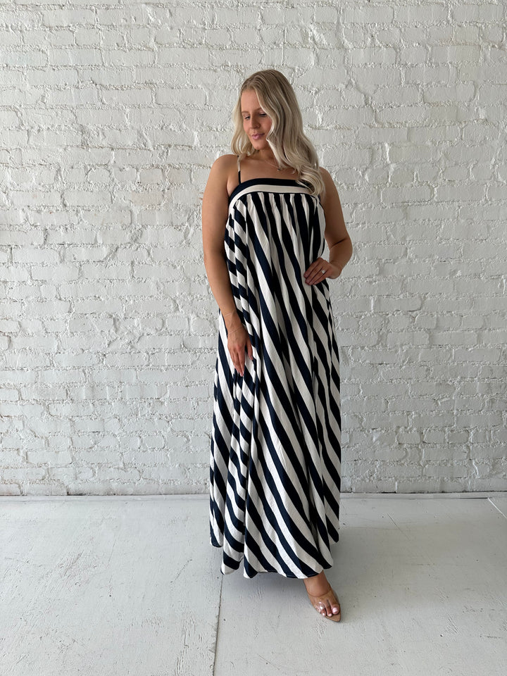 Woman wearing navy and white striped maxi dress with straight neckline and adjustable straps. 
