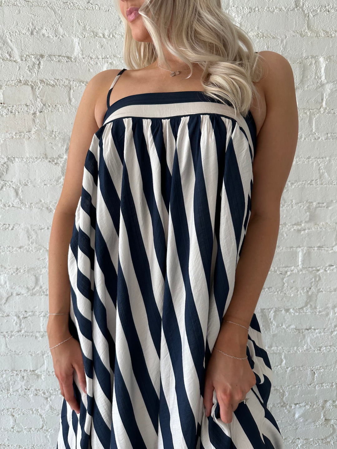 Woman wearing navy and white striped maxi dress with straight neckline and adjustable straps. 