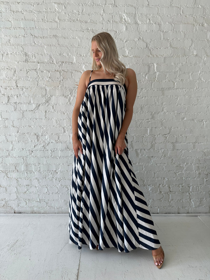Woman wearing navy and white striped maxi dress with straight neckline and adjustable straps. 