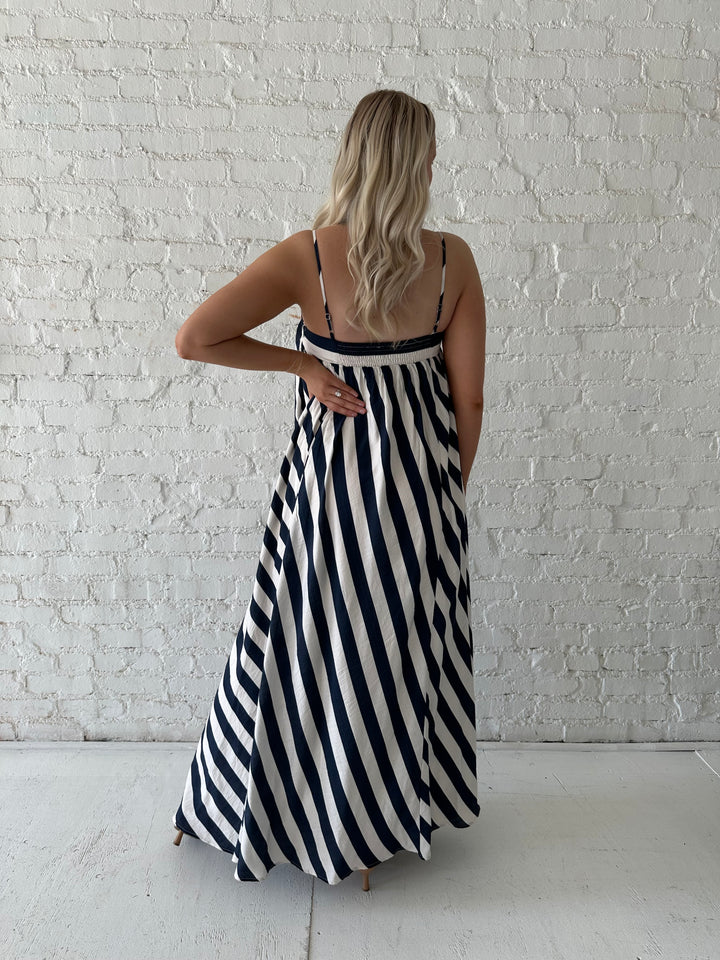 Woman wearing navy and white striped maxi dress with straight neckline and adjustable straps. 