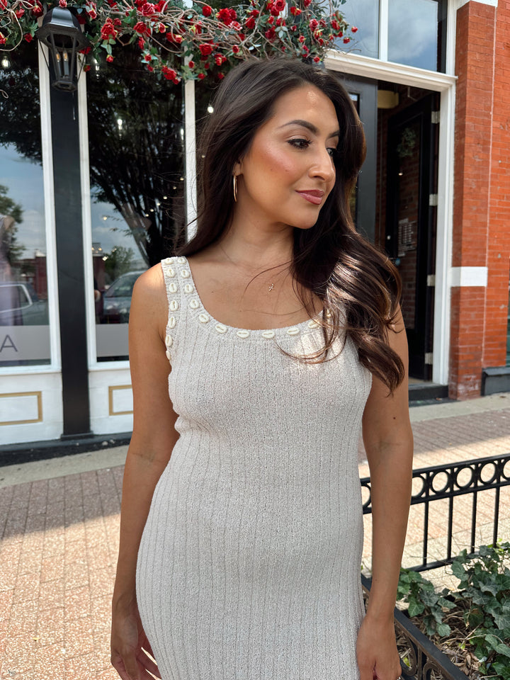 Woman wearing a sleeveless nude knit midi dress with a seashell embellished neckline. 