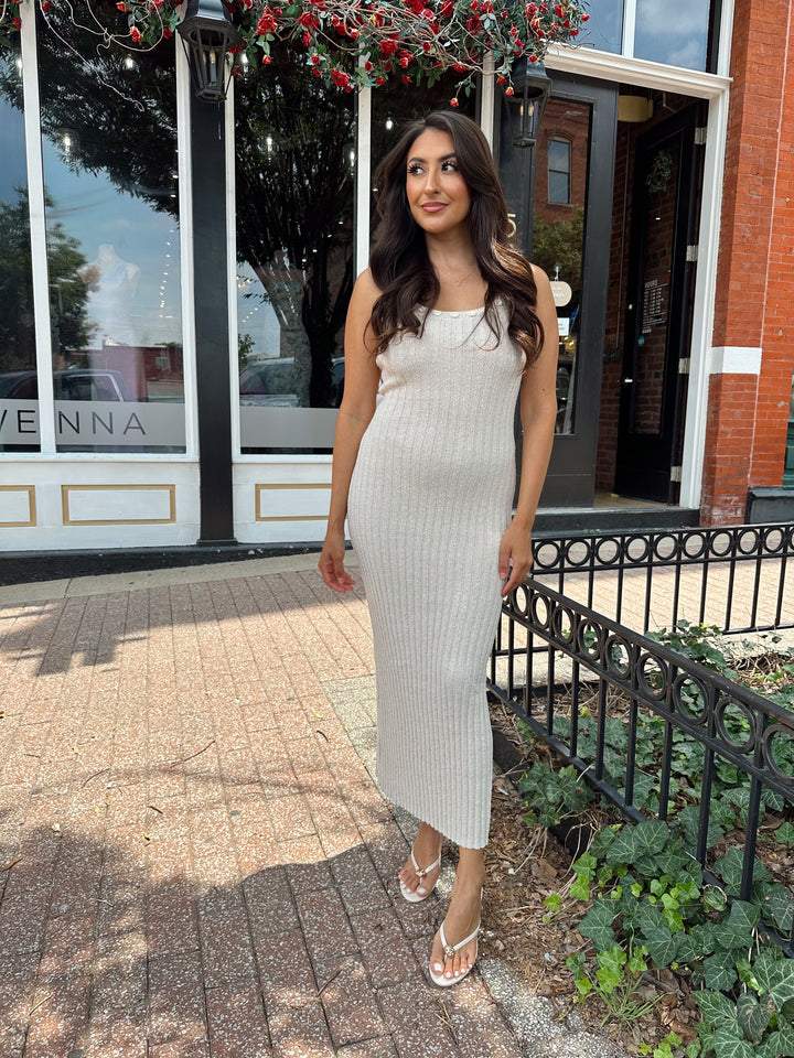 Woman wearing a sleeveless nude knit midi dress with a seashell embellished neckline. 