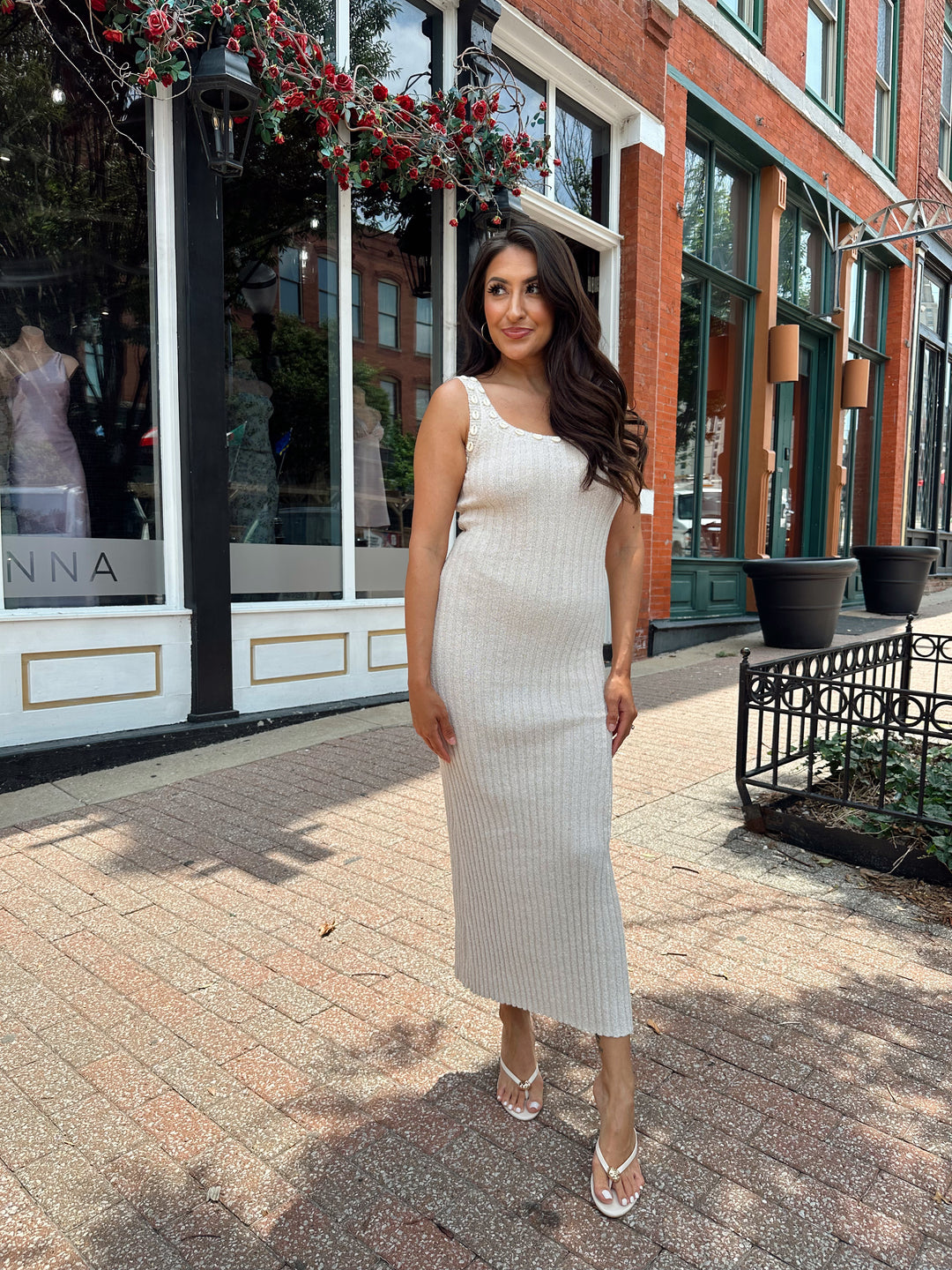Woman wearing a sleeveless nude knit midi dress with a seashell embellished neckline. 