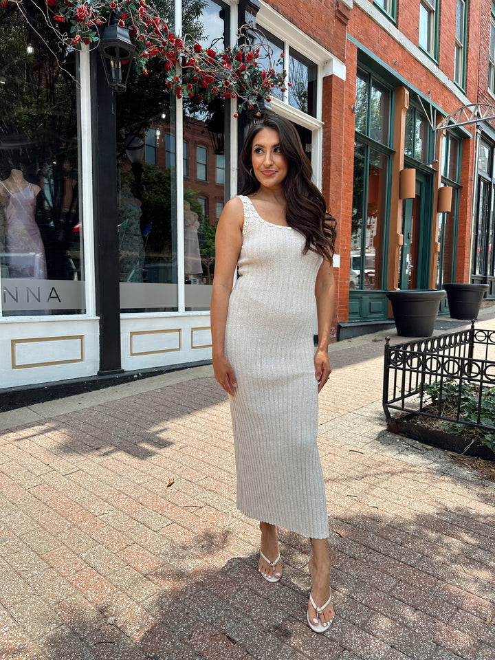 Woman wearing a sleeveless nude knit midi dress with a seashell embellished neckline. 