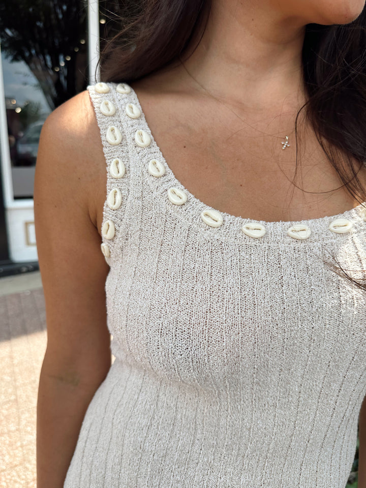 Woman wearing a sleeveless nude knit midi dress with a seashell embellished neckline. 