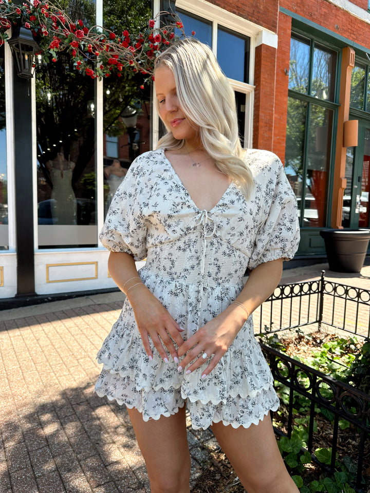 Woman wearing white romper with black floral pattern, tiered short. 