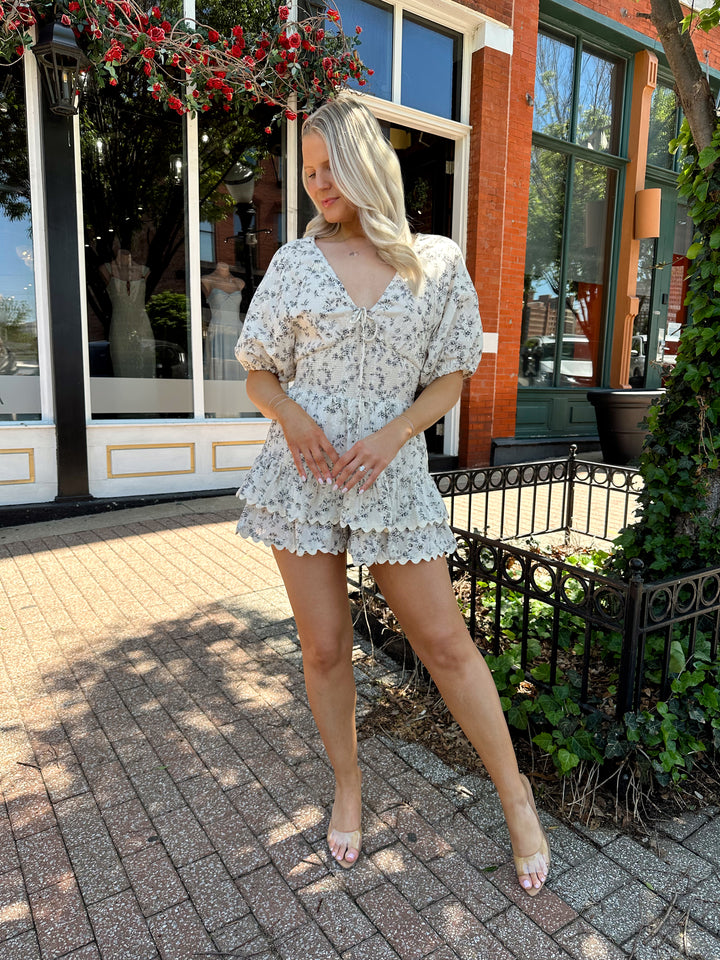 Woman wearing white romper with black floral pattern, tiered short. 