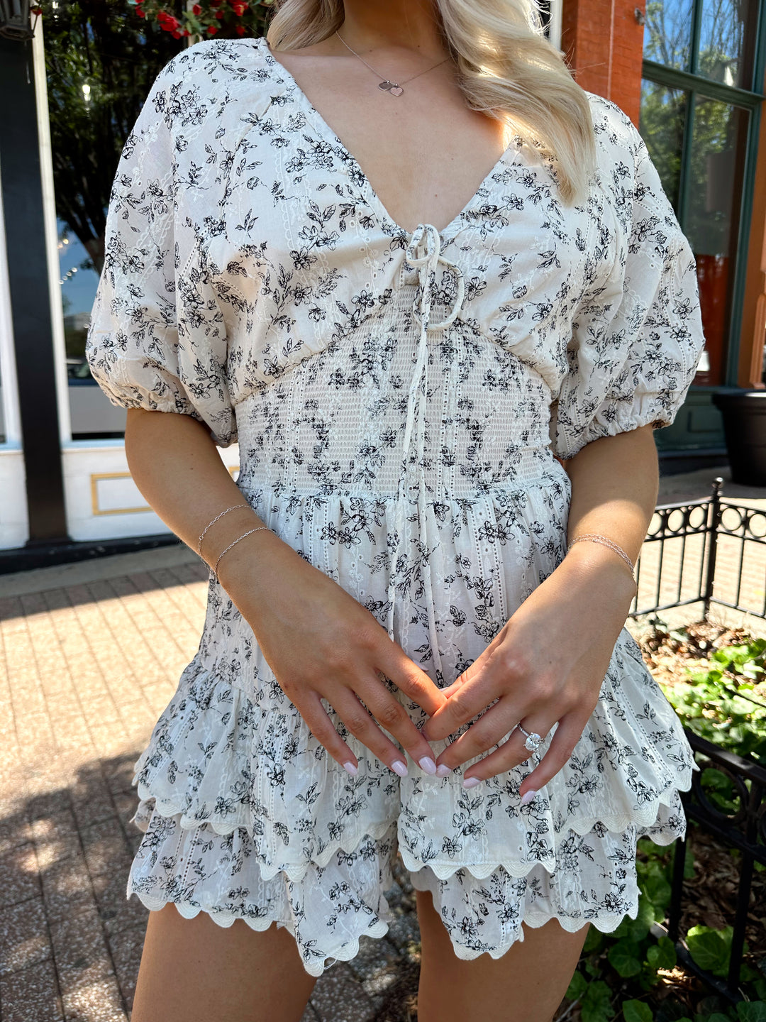 Woman wearing white romper with black floral pattern, tiered short. 