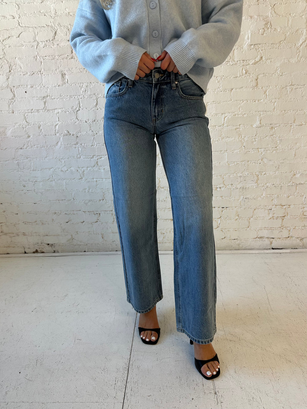 Woman wearing medium wash, mid rise, wide leg jean with a blue button down cardigan. 