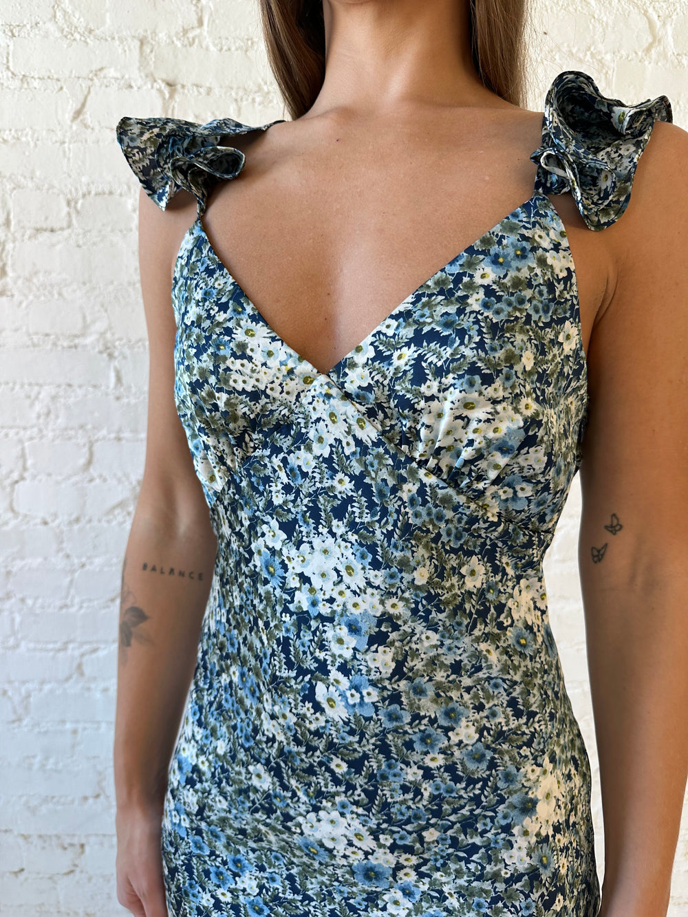 Woman wearing blue floral satin maxi dress with v-neckline, ruffle, adjustable spaghetti straps, and open back. 