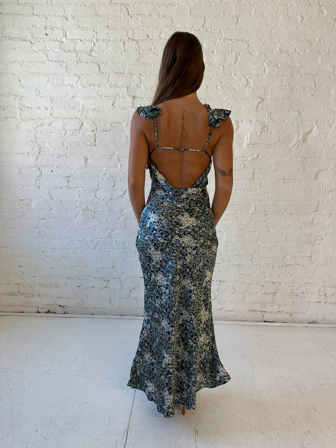Woman wearing blue floral satin maxi dress with v-neckline, ruffle, adjustable spaghetti straps, and open back. 