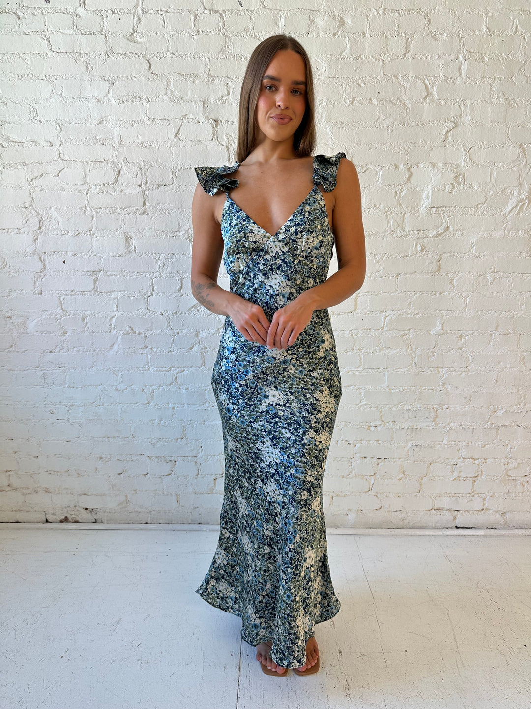 Woman wearing blue floral satin maxi dress with v-neckline, ruffle, adjustable spaghetti straps, and open back. 