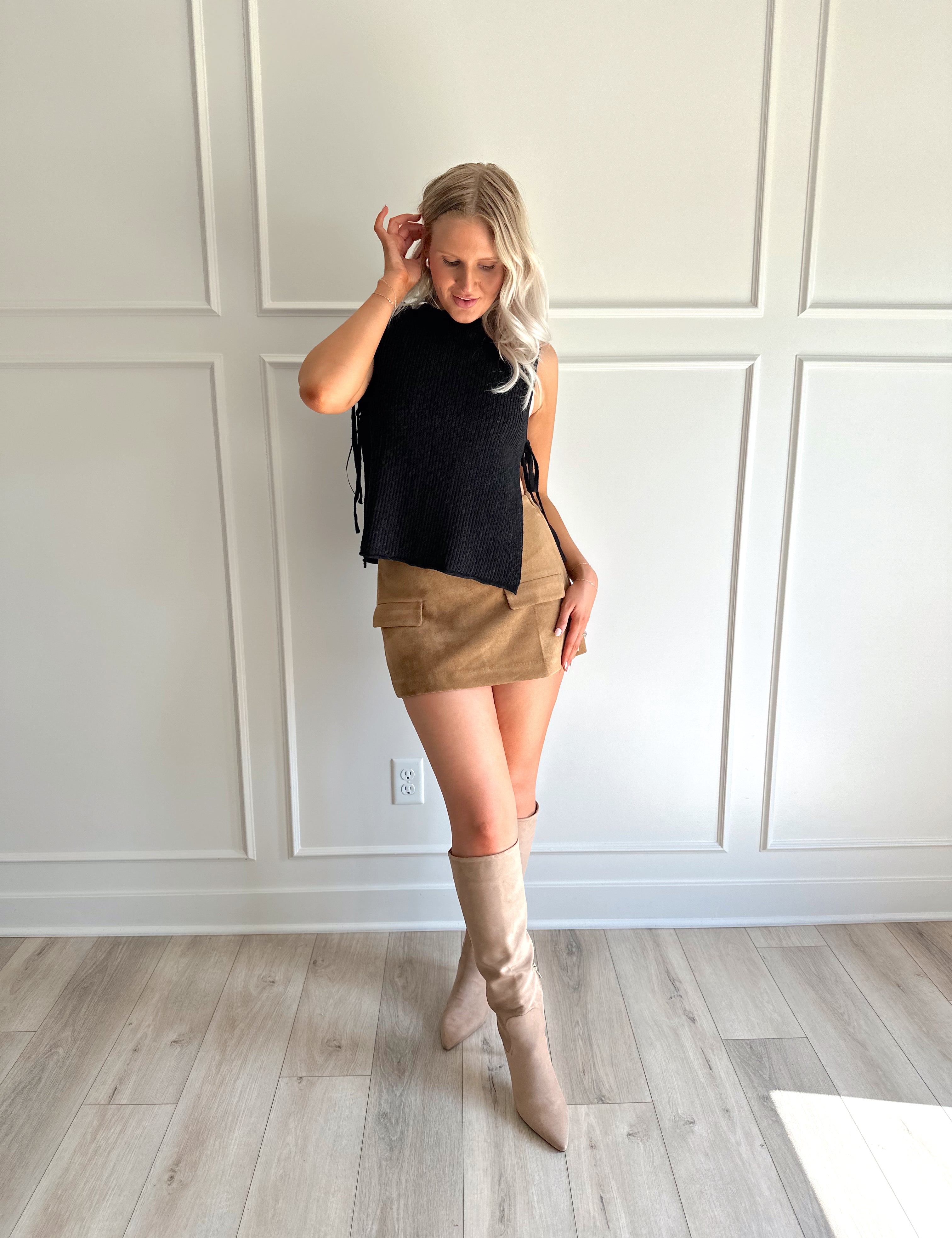 Woman wearing a black knit sleeveless sweater top with tie side detail.