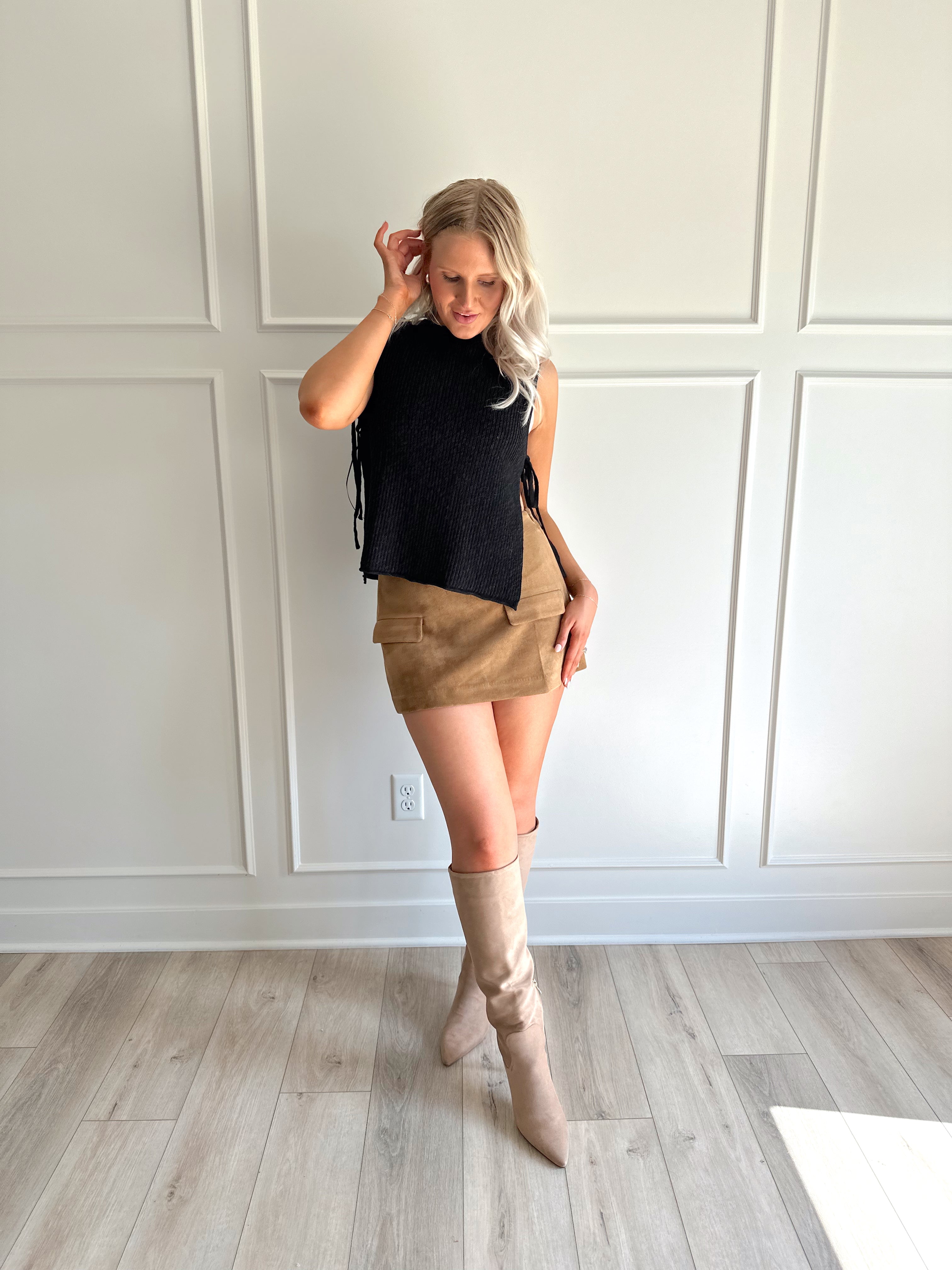 Woman wearing a black knit sleeveless sweater top with tie side detail.