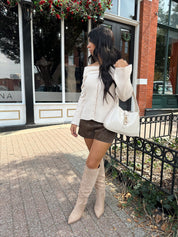Woman wearing cream off the shoulder long sleeve ribbed top with button detail.