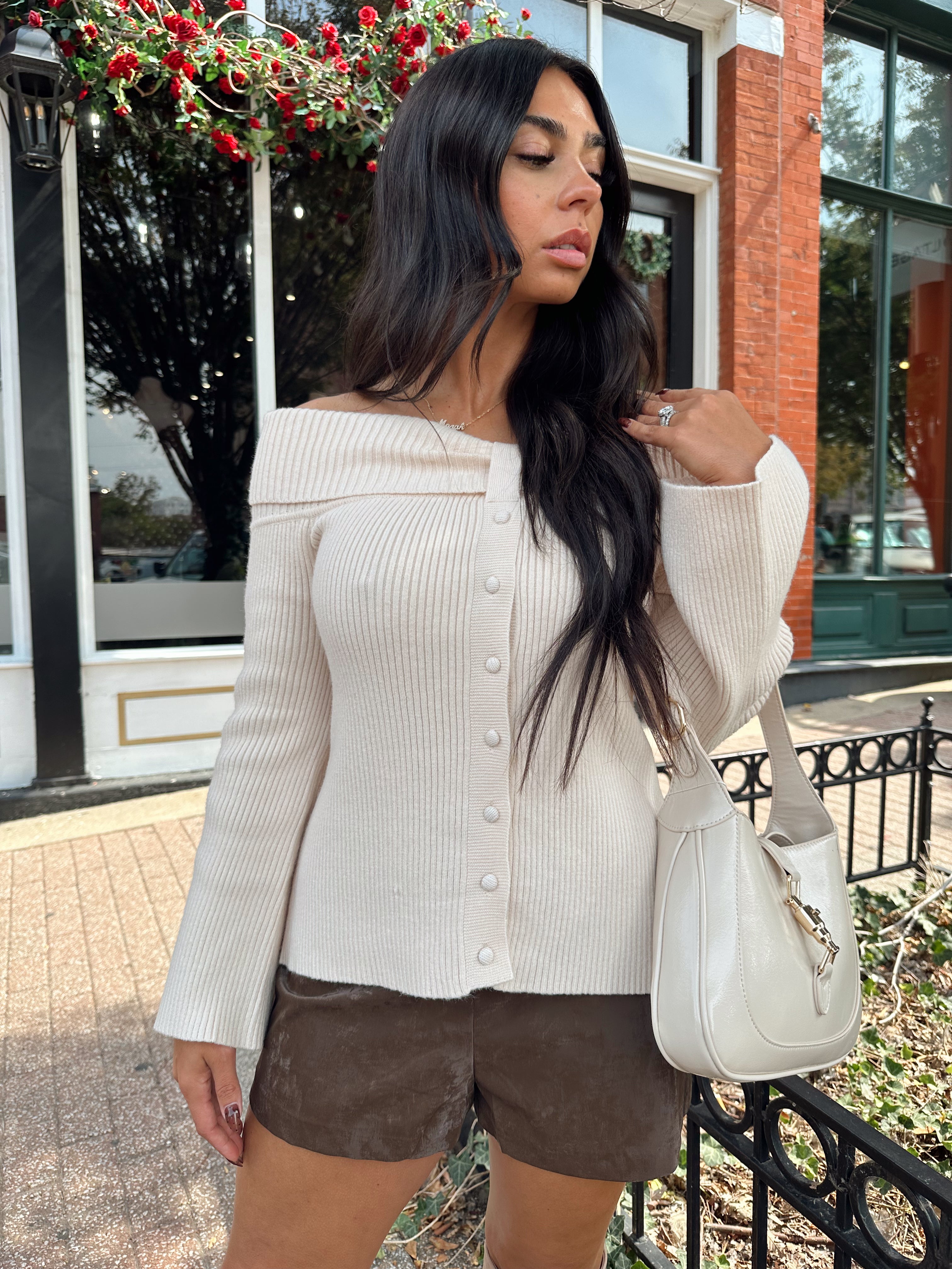 Woman wearing cream off the shoulder long sleeve ribbed top with button detail.