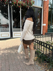 Woman wearing cream off the shoulder long sleeve ribbed top with button detail.
