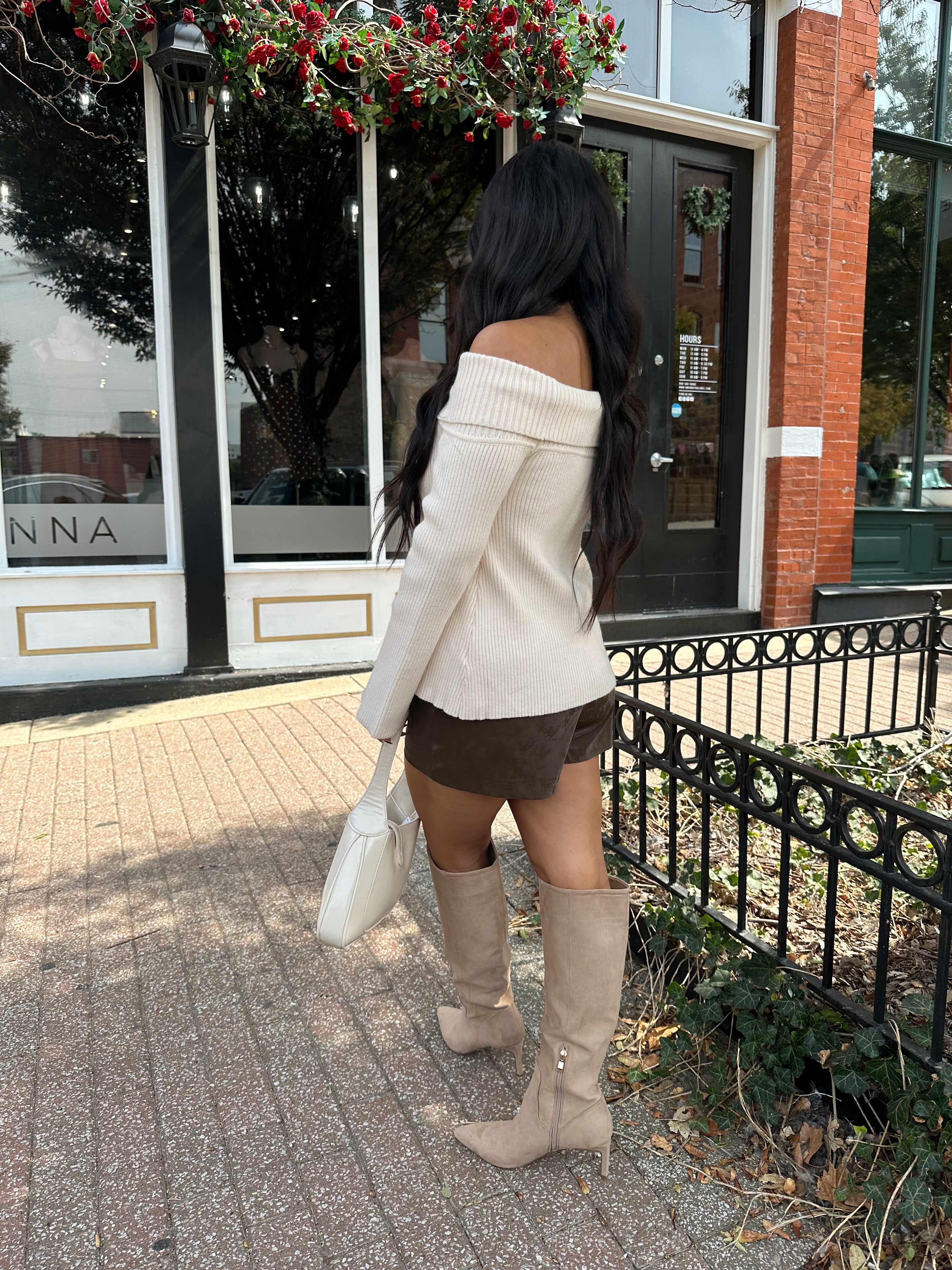 Woman wearing cream off the shoulder long sleeve ribbed top with button detail.