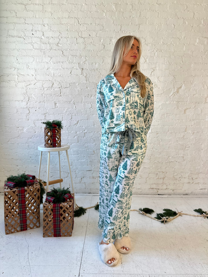 Woman wearing green and white pattern satin pajama set with long sleeve button down top, and long pants.