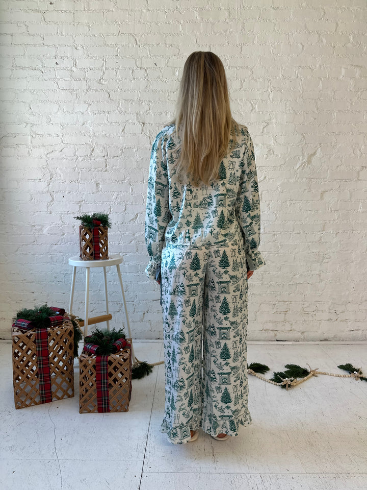 Woman wearing green and white pattern satin pajama set with long sleeve button down top, and long pants.