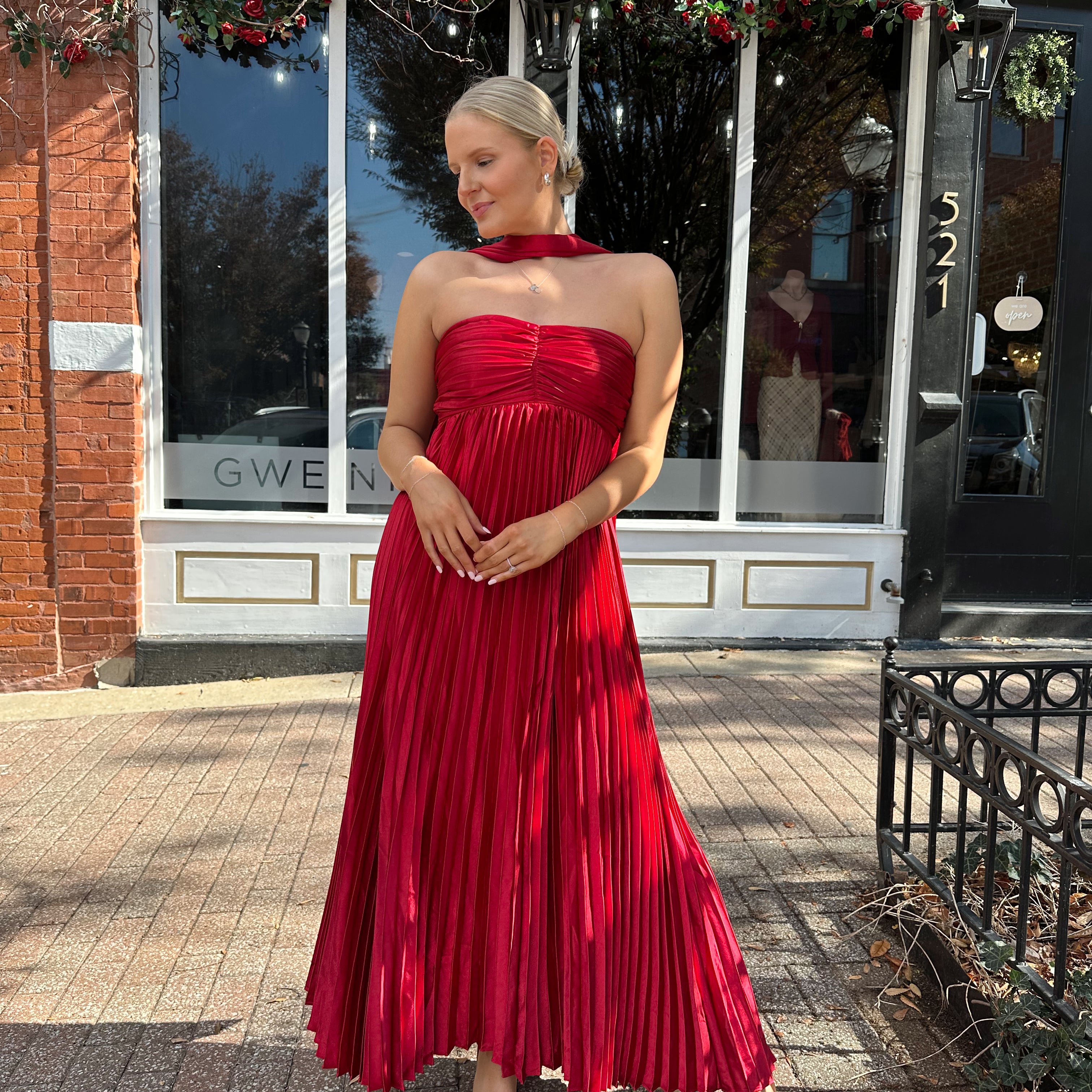Woman wearing strapless red plissé maxi dress with lace up back, and detachable scarf.