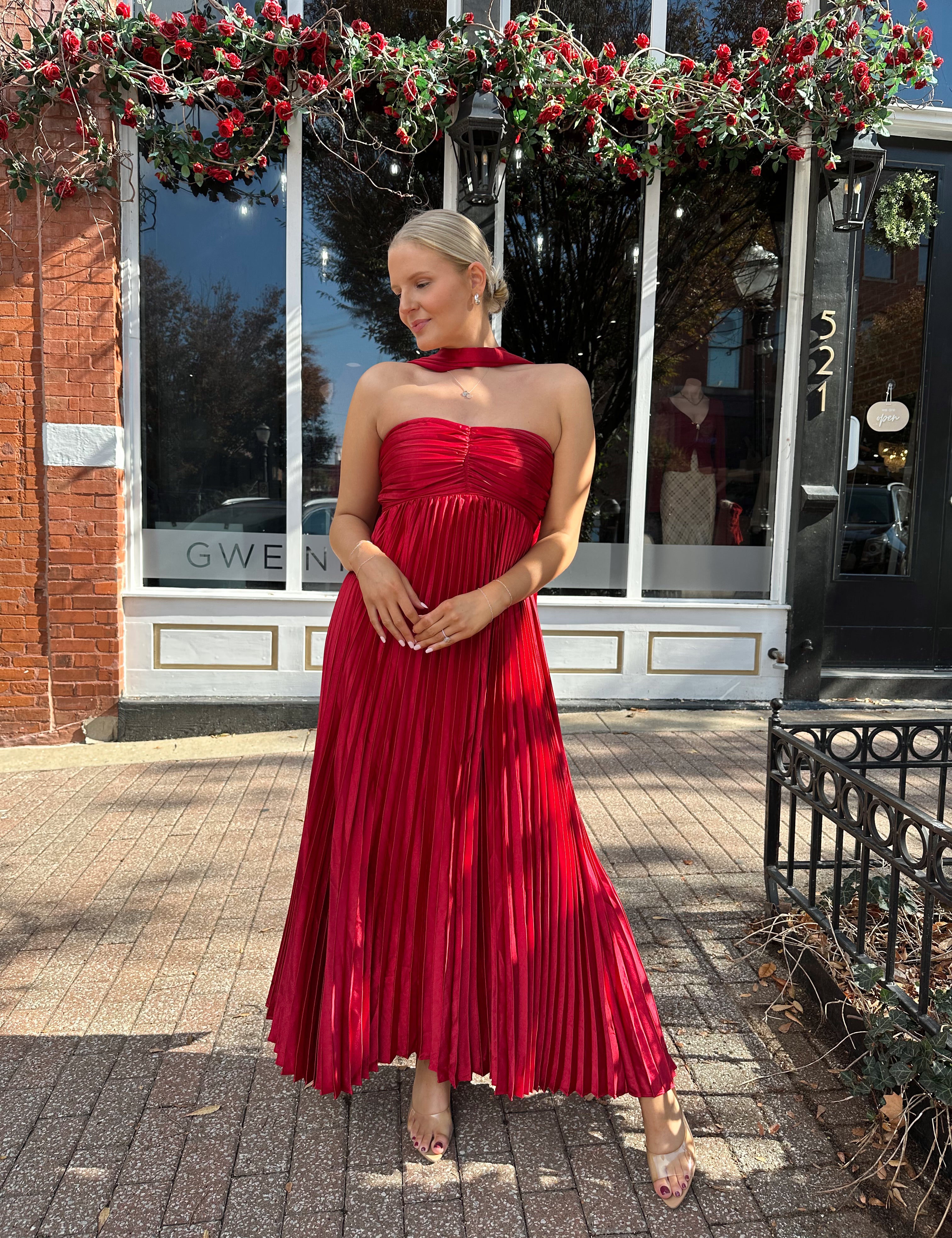 Woman wearing strapless red plissé maxi dress with lace up back, and detachable scarf.