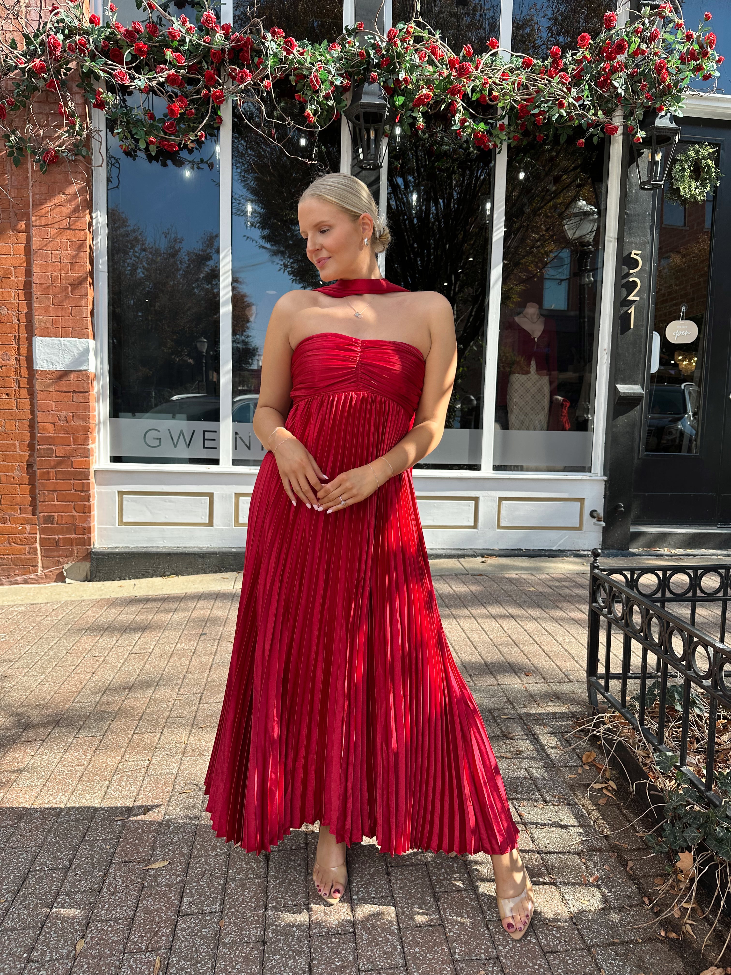 Woman wearing strapless red plissé maxi dress with lace up back, and detachable scarf.