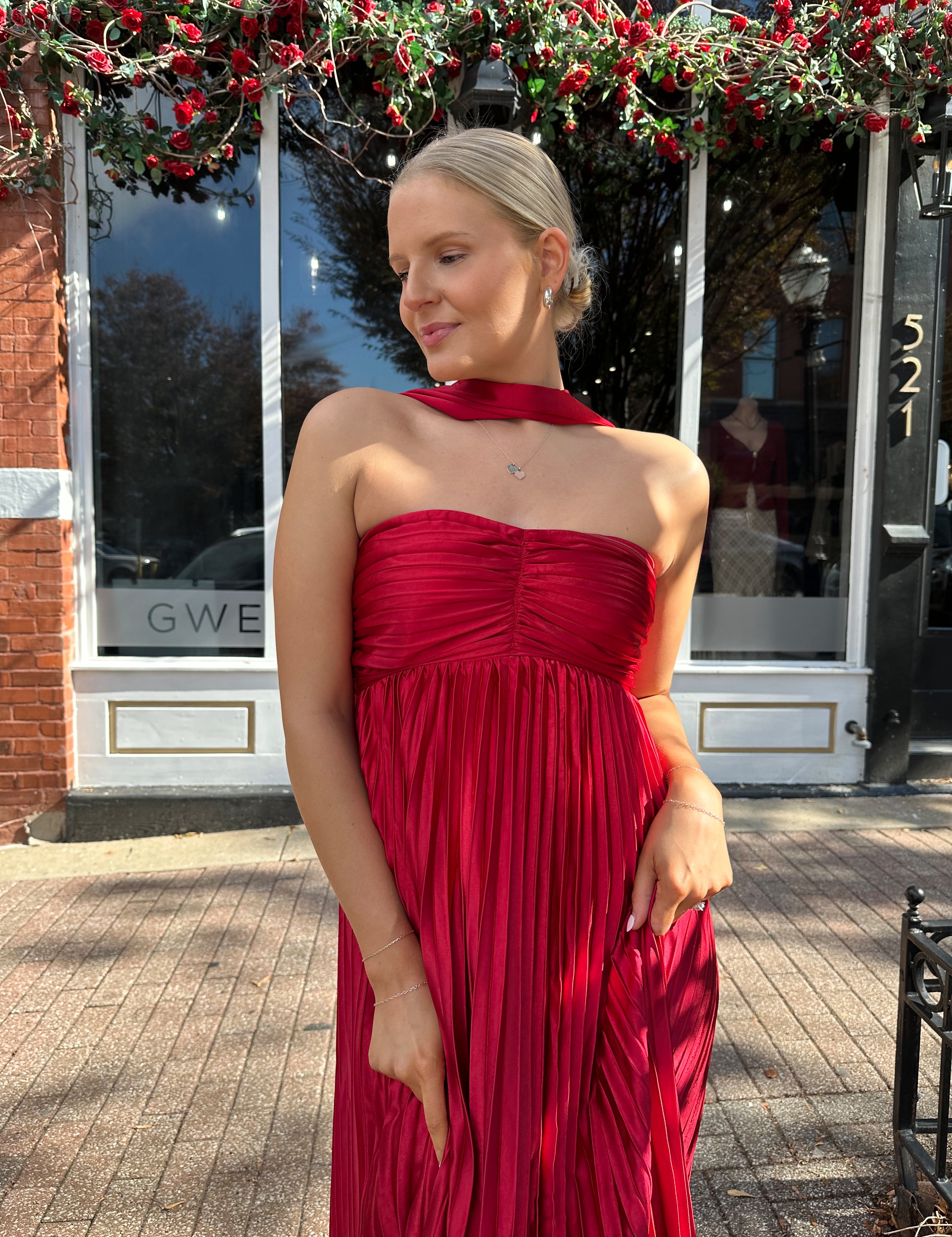Woman wearing strapless red plissé maxi dress with lace up back, and detachable scarf.