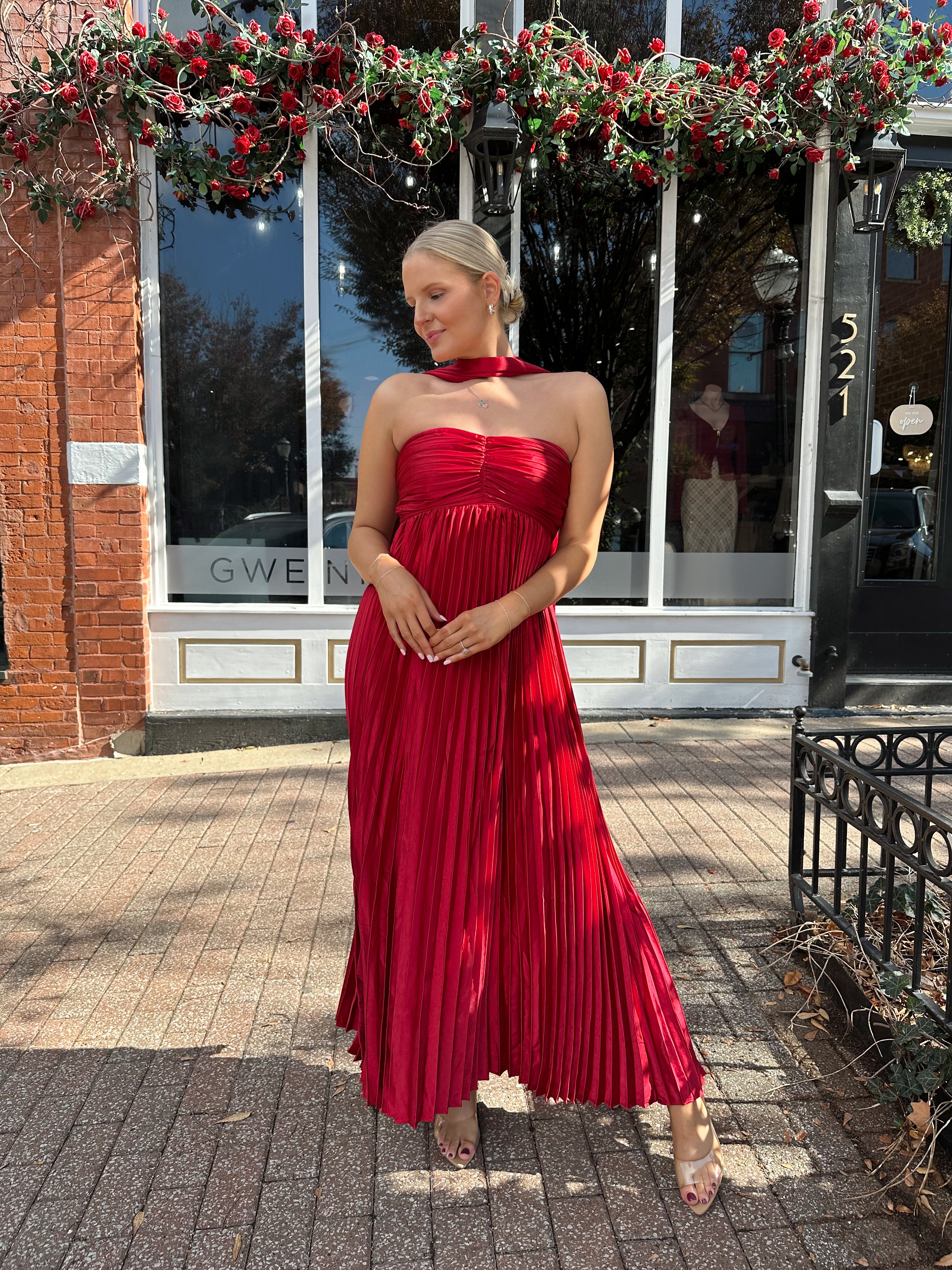 Woman wearing strapless red plissé maxi dress with lace up back, and detachable scarf.