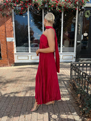 Woman wearing strapless red plissé maxi dress with lace up back, and detachable scarf.