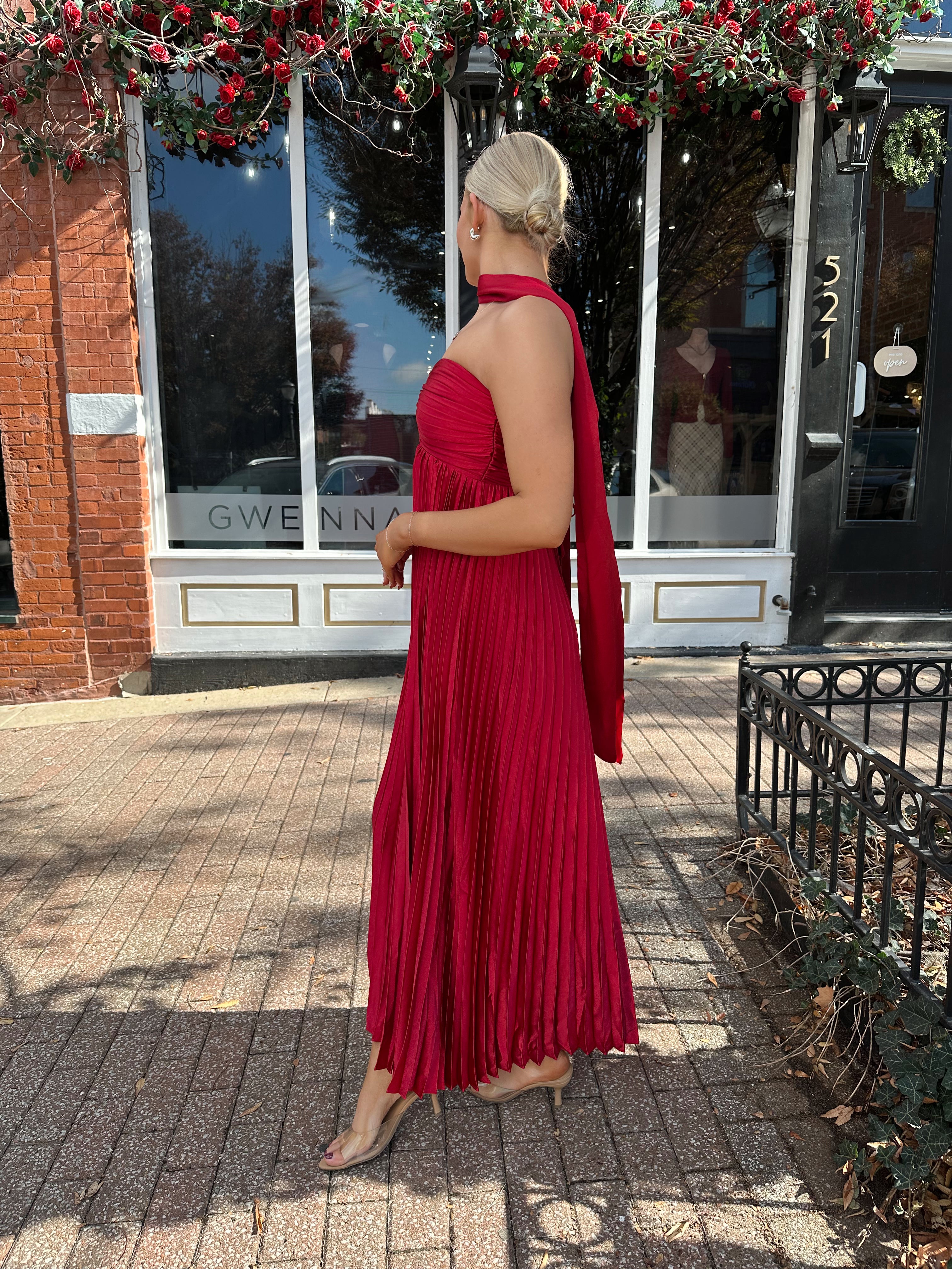 Woman wearing strapless red plissé maxi dress with lace up back, and detachable scarf.