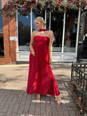 Woman wearing strapless red plissé maxi dress with lace up back, and detachable scarf.
