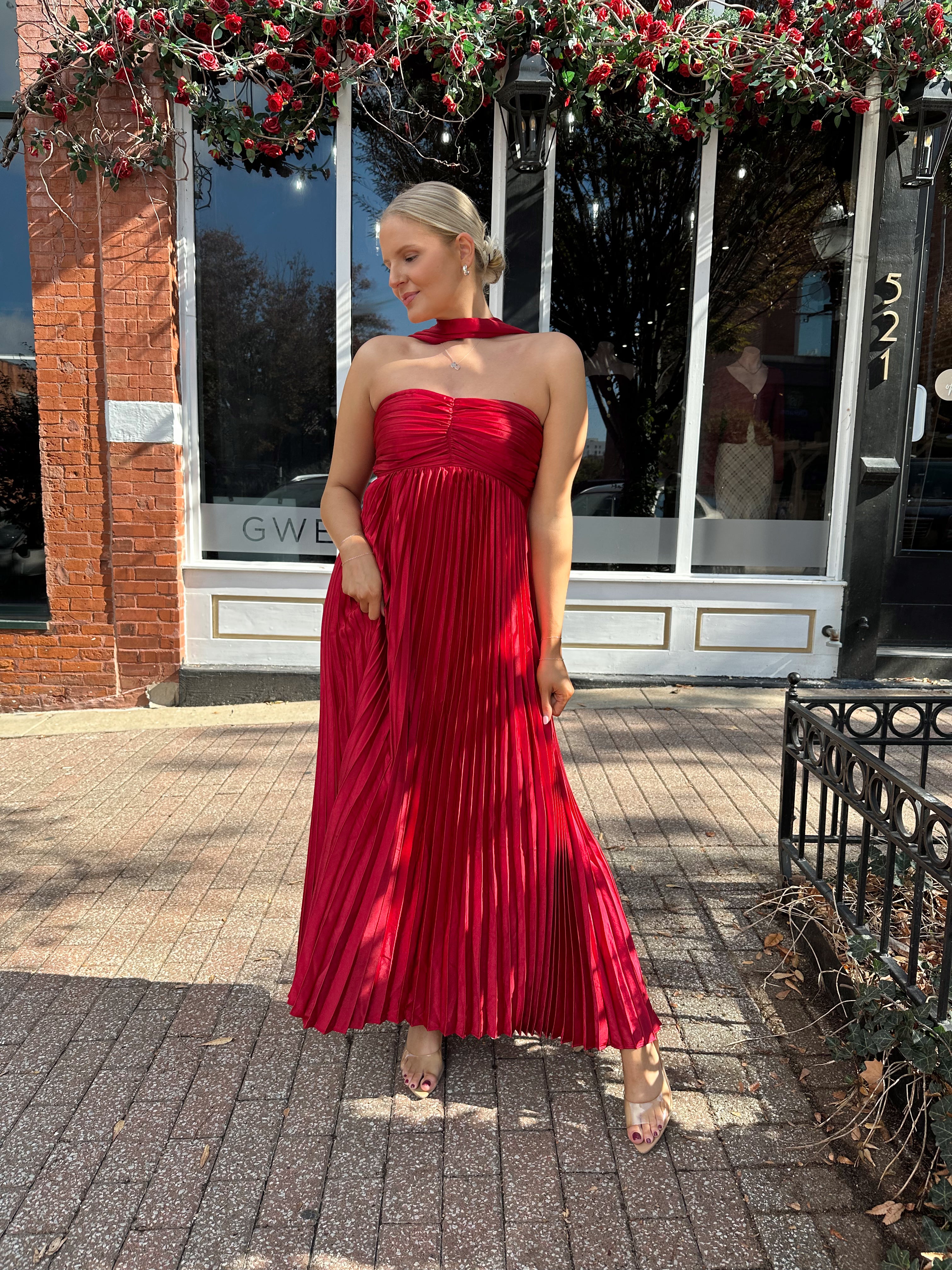 Woman wearing strapless red plissé maxi dress with lace up back, and detachable scarf.