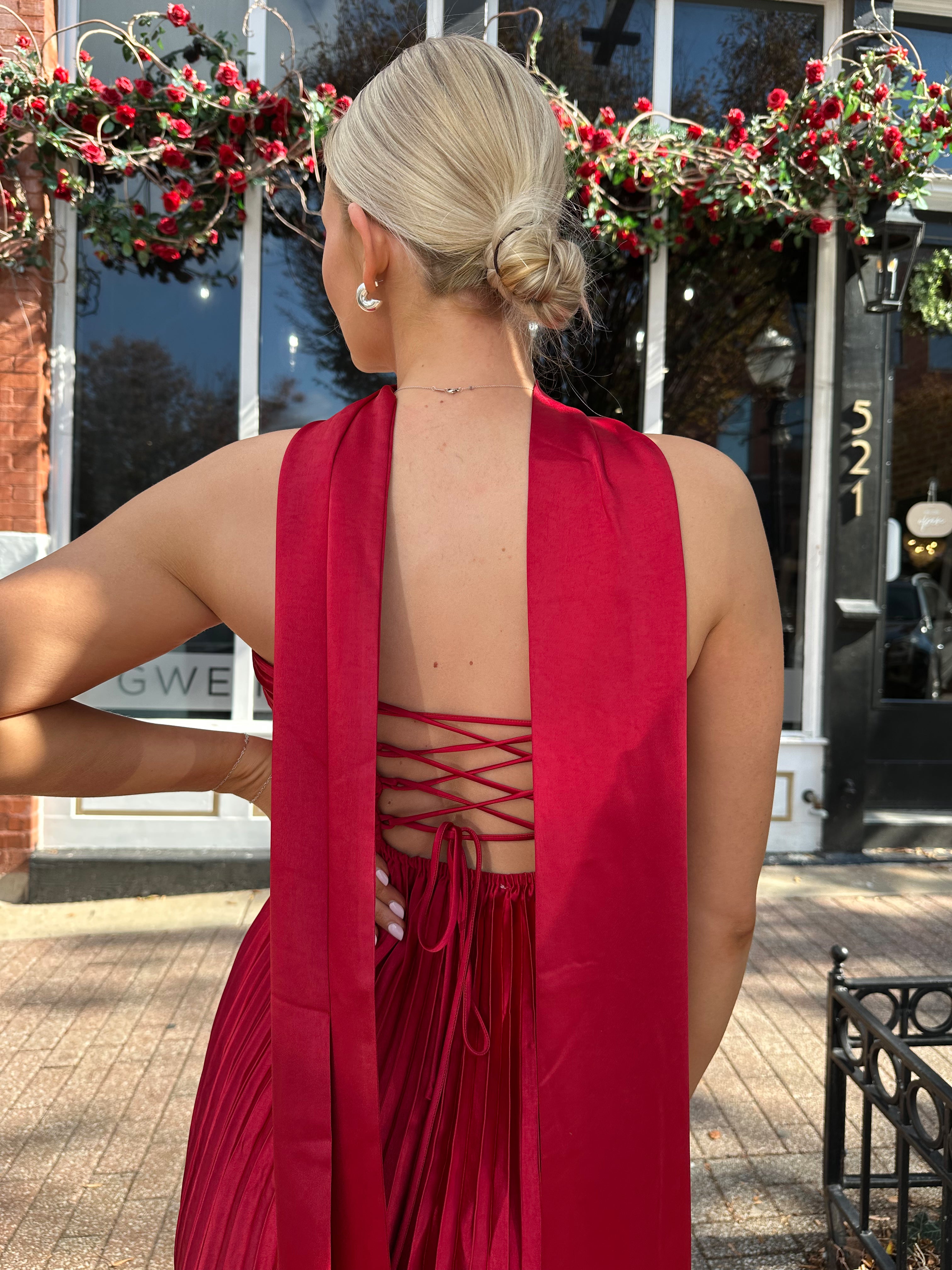 Woman wearing strapless red plissé maxi dress with lace up back, and detachable scarf.
