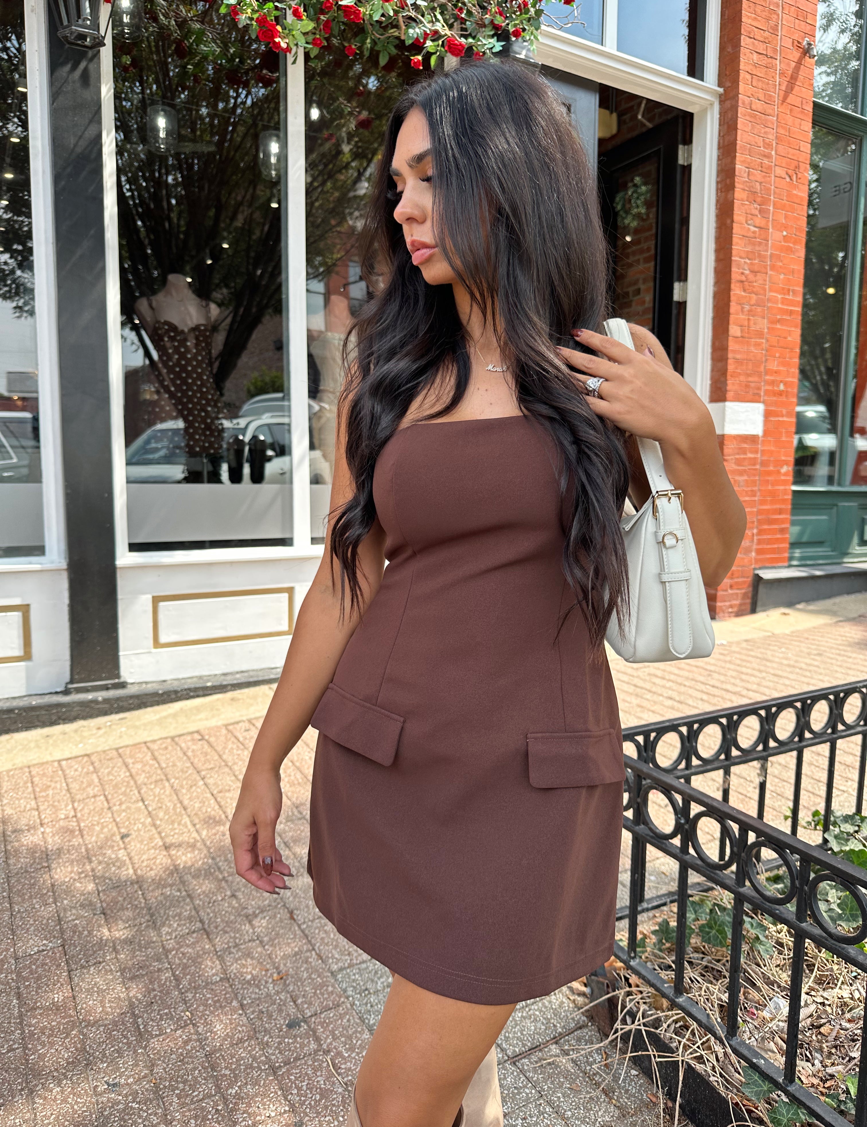 Woman wearing dark brown tailored mini dress with front pockets and built in shorts. 