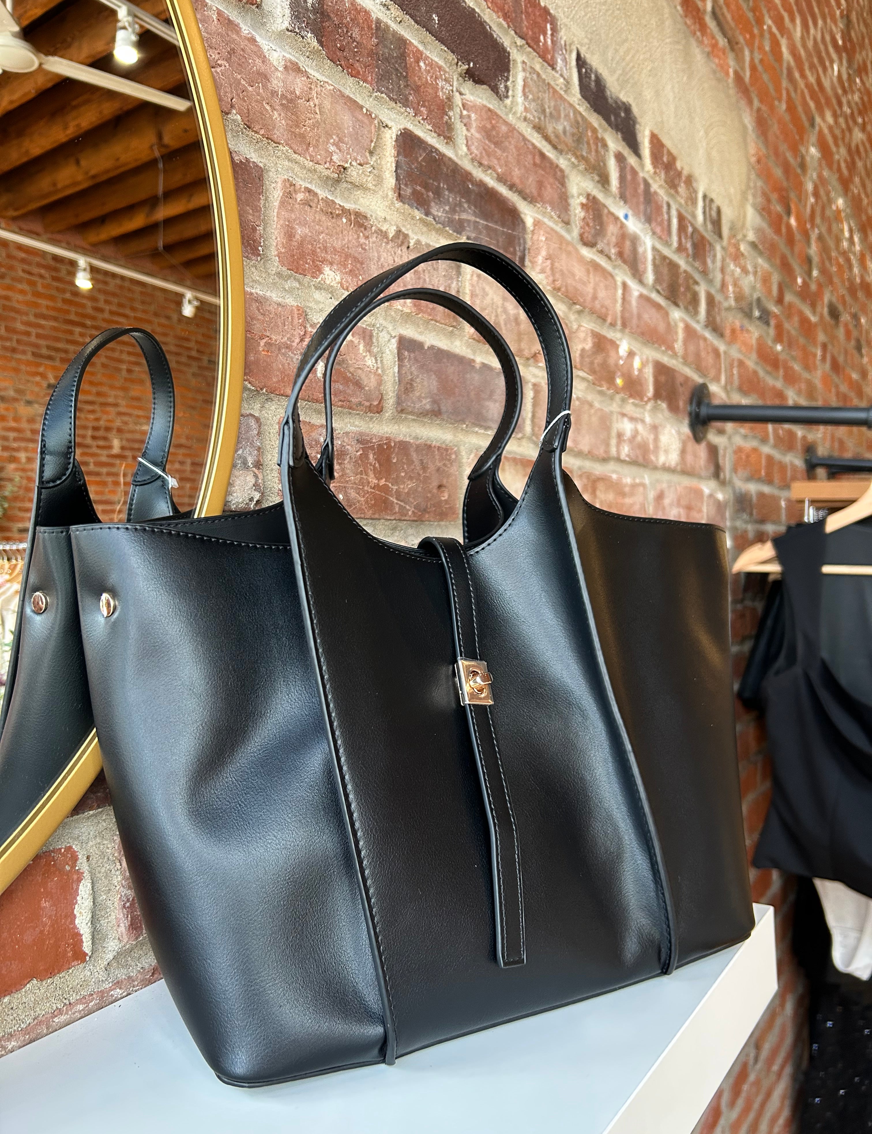 Black vegan leather tote bag with gold hardware and structured handles displayed on boutique shelf.