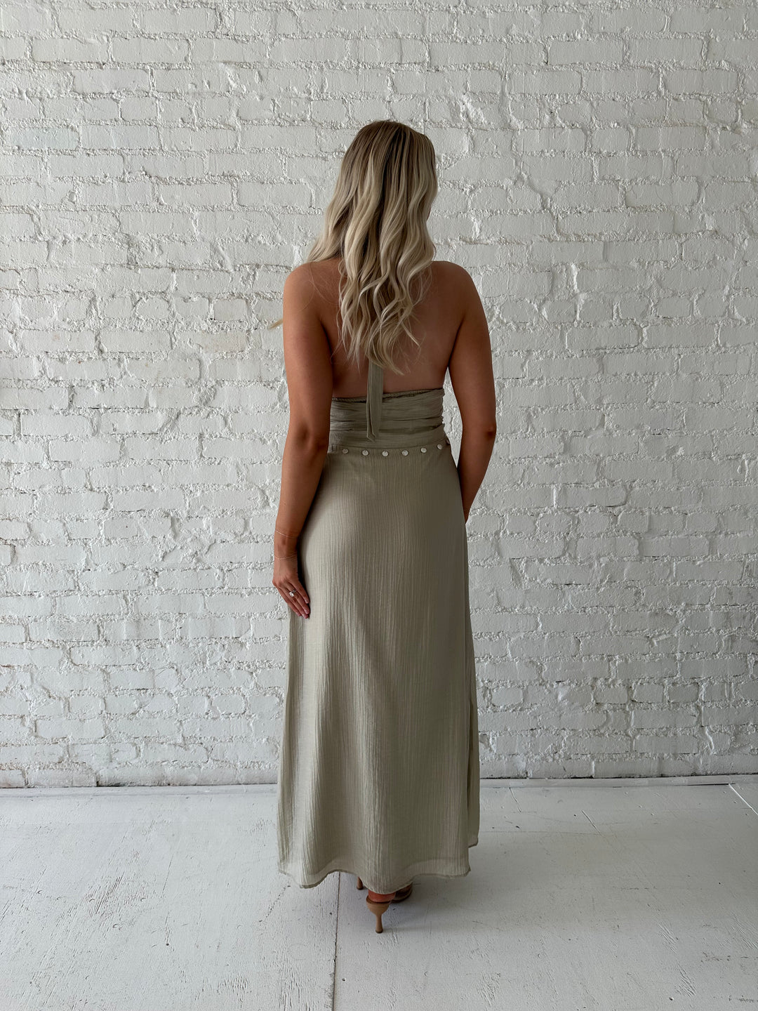 Woman wearing khaki colored maxi dress with halter neckline, and shell trim detailing. 