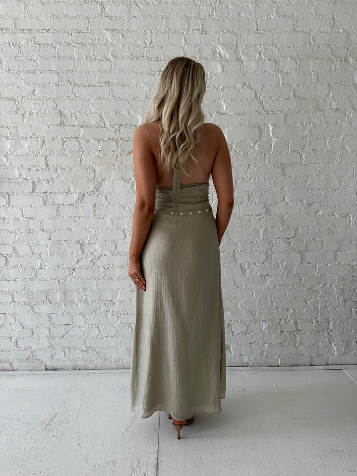 Woman wearing khaki colored maxi dress with halter neckline, and shell trim detailing. 