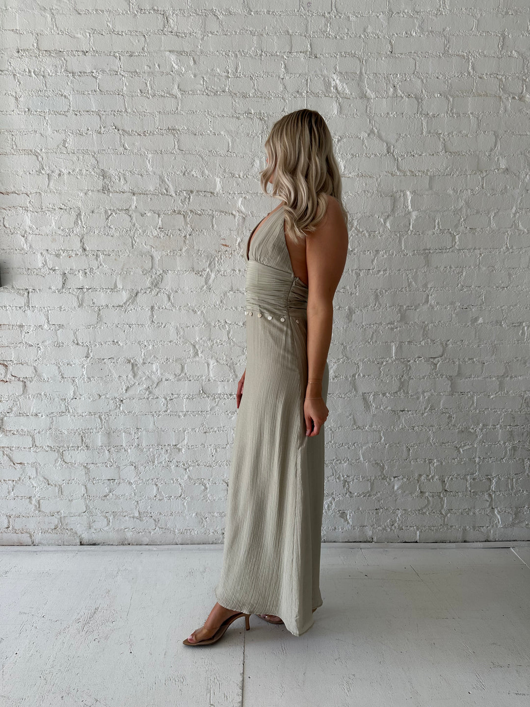Woman wearing khaki colored maxi dress with halter neckline, and shell trim detailing. 