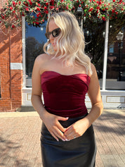Woman wearing burgundy velvet strapless top with satin neckline. 