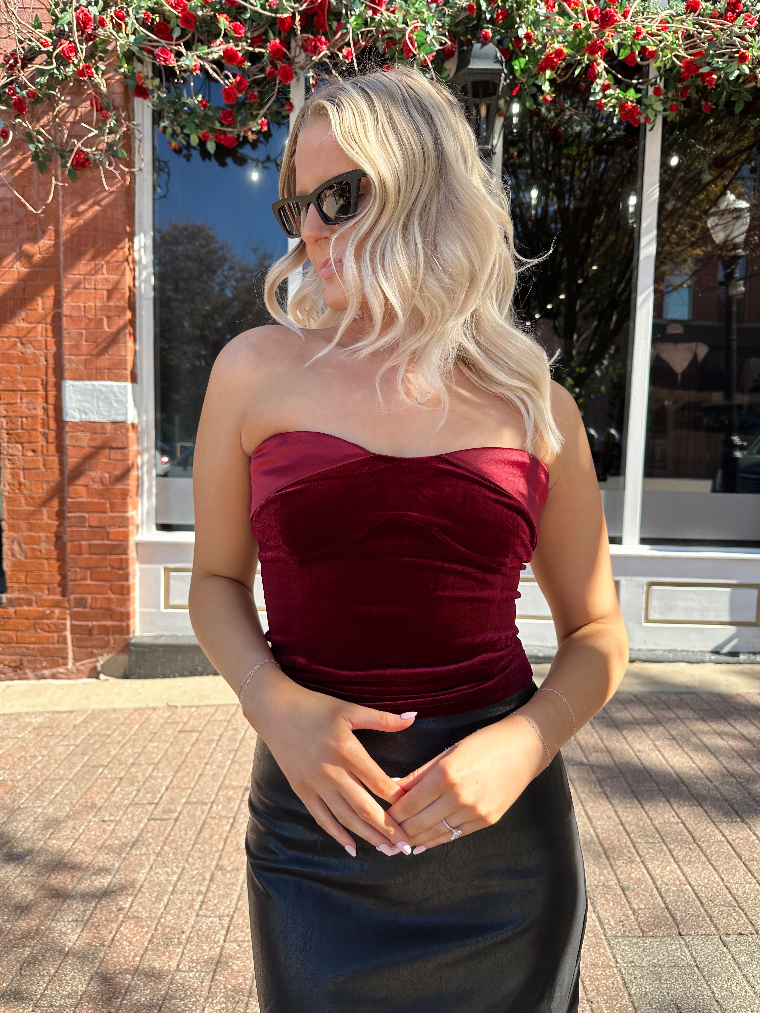 Woman wearing burgundy velvet strapless top with satin neckline. 