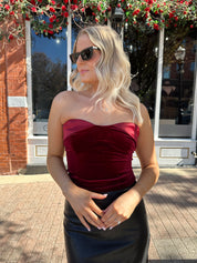 Woman wearing burgundy velvet strapless top with satin neckline. 
