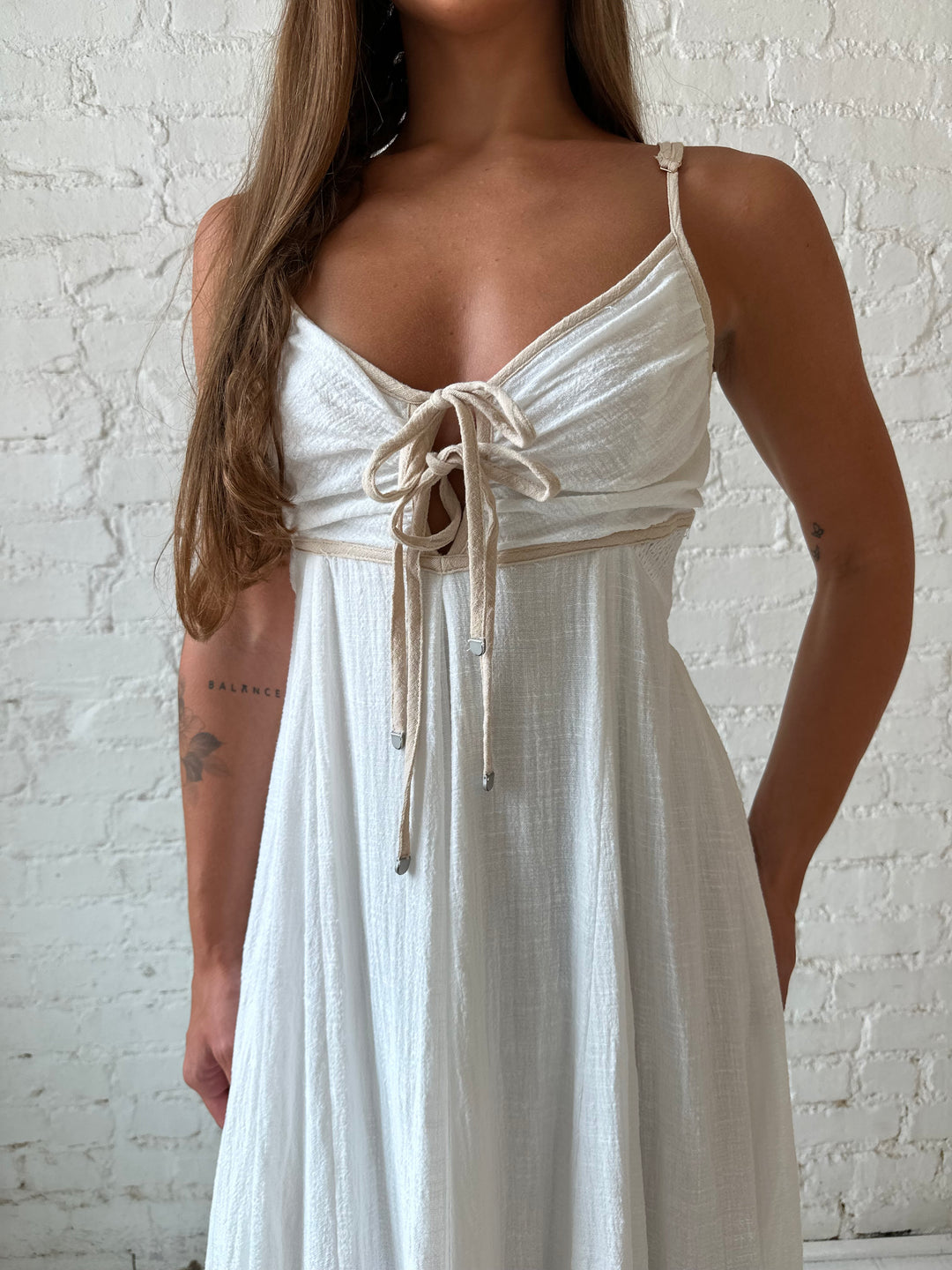 Woman wearing white flowy maxi dress with tan trim detailing. 