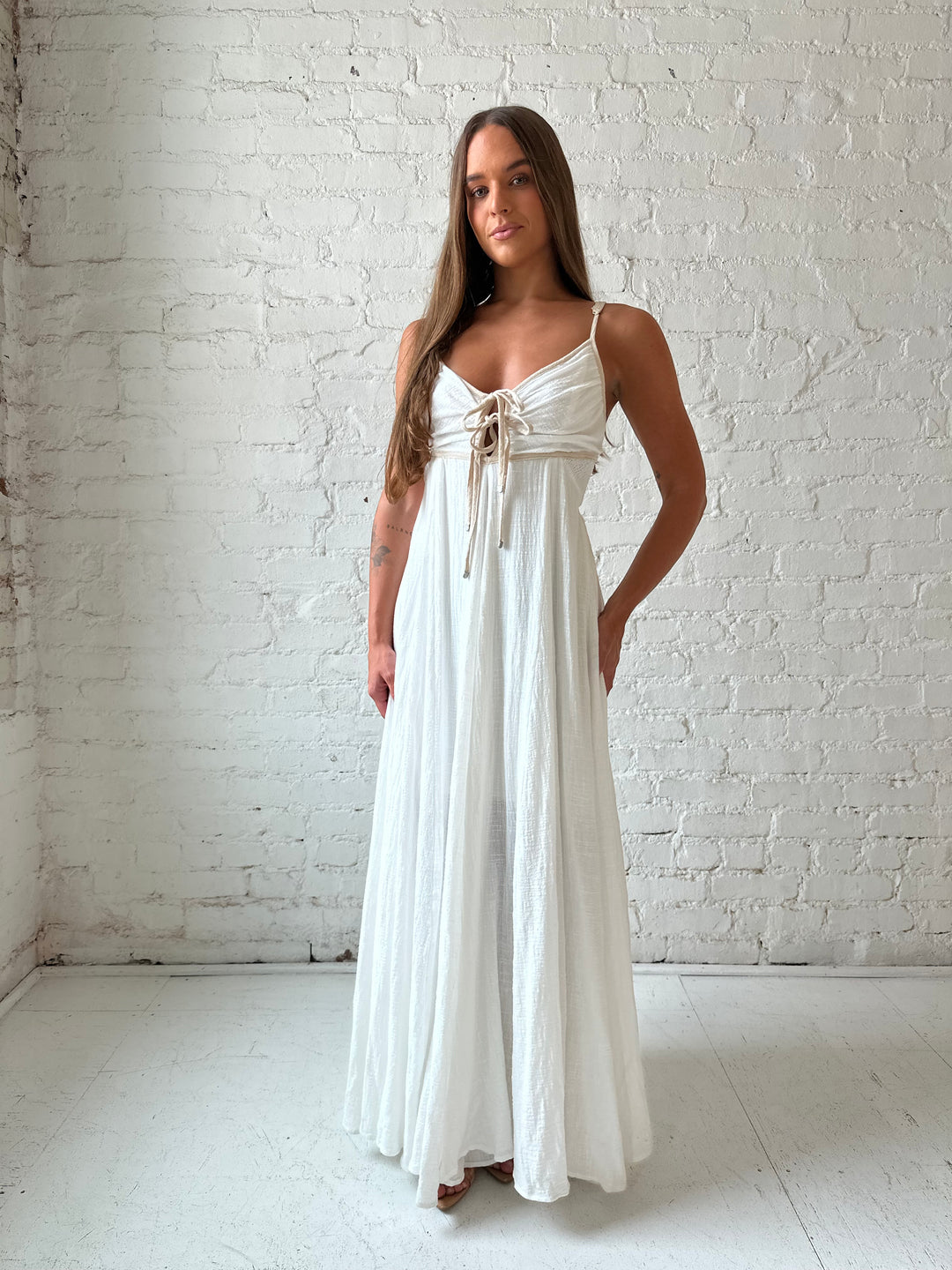 Woman wearing white flowy maxi dress with tan trim detailing. 