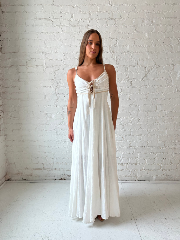 Woman wearing white flowy maxi dress with tan trim detailing. 