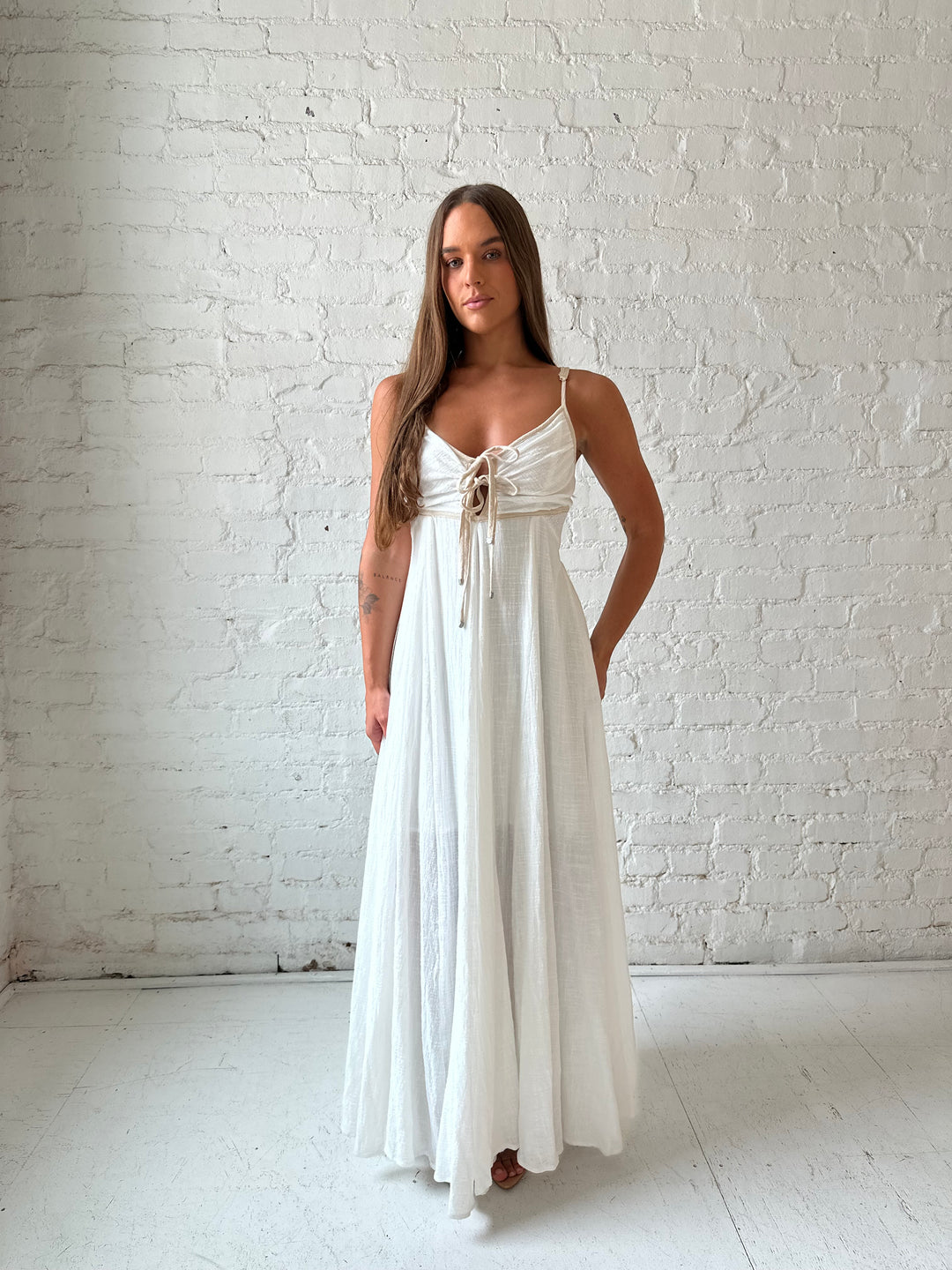 Woman wearing white flowy maxi dress with tan trim detailing. 