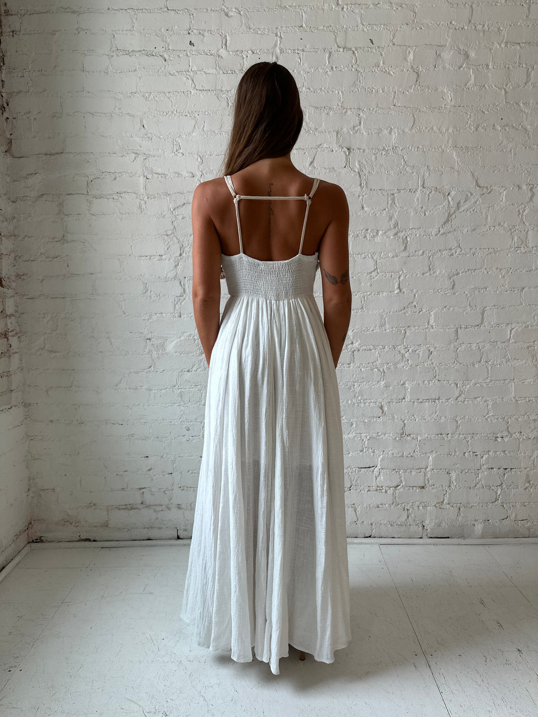 Woman wearing white flowy maxi dress with tan trim detailing. 