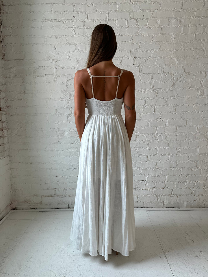 Woman wearing white flowy maxi dress with tan trim detailing. 