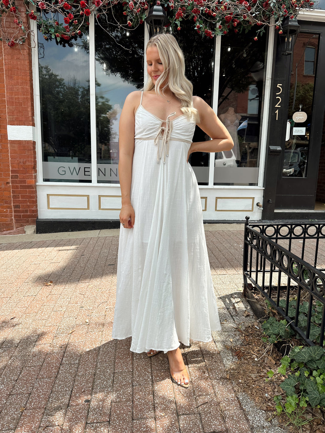 Woman wearing white flowy maxi dress with tan trim detailing. 